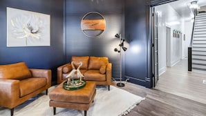 A modern living room with a dark blue accent wall, a brown leather sofa, a coffee table with a decorative bird sculpture, a floor lamp, and a framed artwork. - 6BR Gem in Midtown Atlanta (Atlanta)