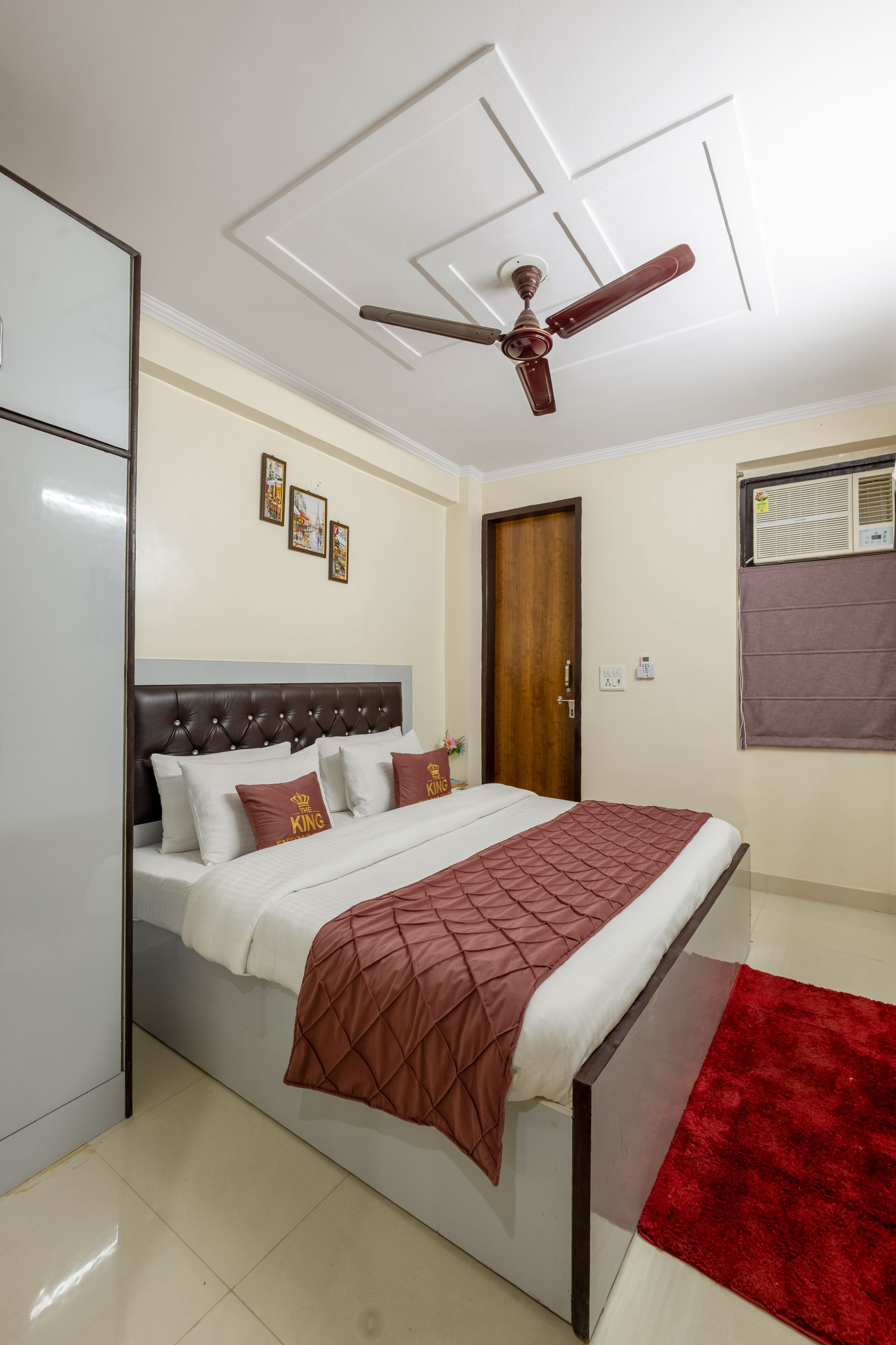 A bedroom with a bed, a ceiling fan, a wooden door, and a window with an air conditioning unit.