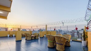A rooftop terrace with wicker chairs, potted plants, and a white fence. - The King Residency (New Delhi)