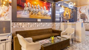 A reception area with a sofa, chairs, a reception desk, and a ceiling fan. - The King Residency (New Delhi)