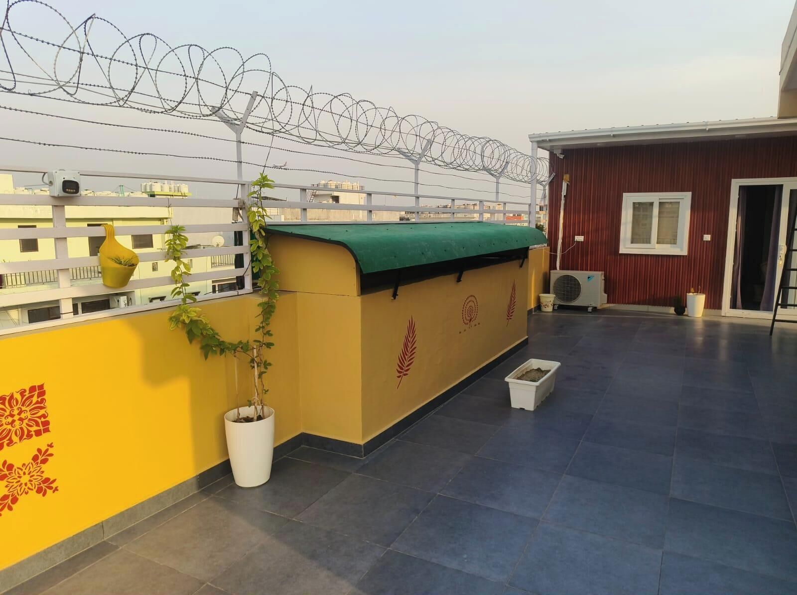 A rooftop terrace with a yellow wall, a green awning, and a white planter with a plant.
