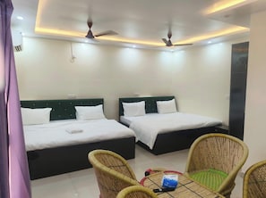 A hotel room with two beds, ceiling fans, a table with chairs, and a wall-mounted air conditioner. - The King Residency (New Delhi)