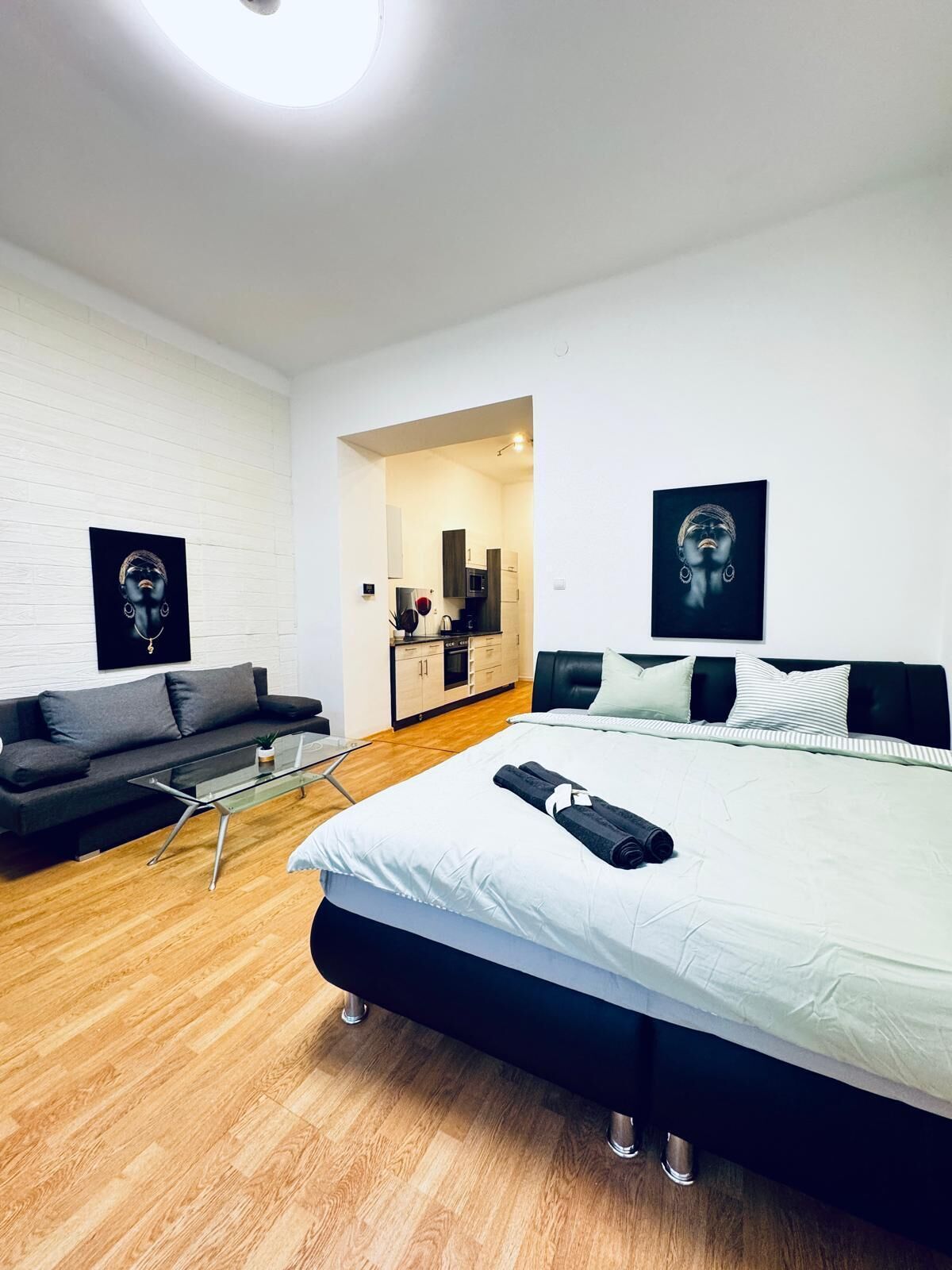 Una habitación de hotel moderna con una cama grande, un sofá, una pequeña mesa y una kitchenette al fondo.