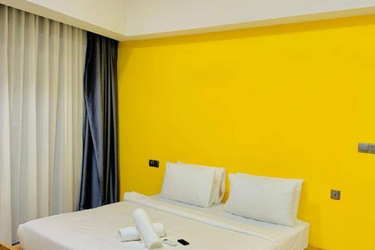 A hotel room with a bed, curtains, a ceiling fan, and a yellow wall.