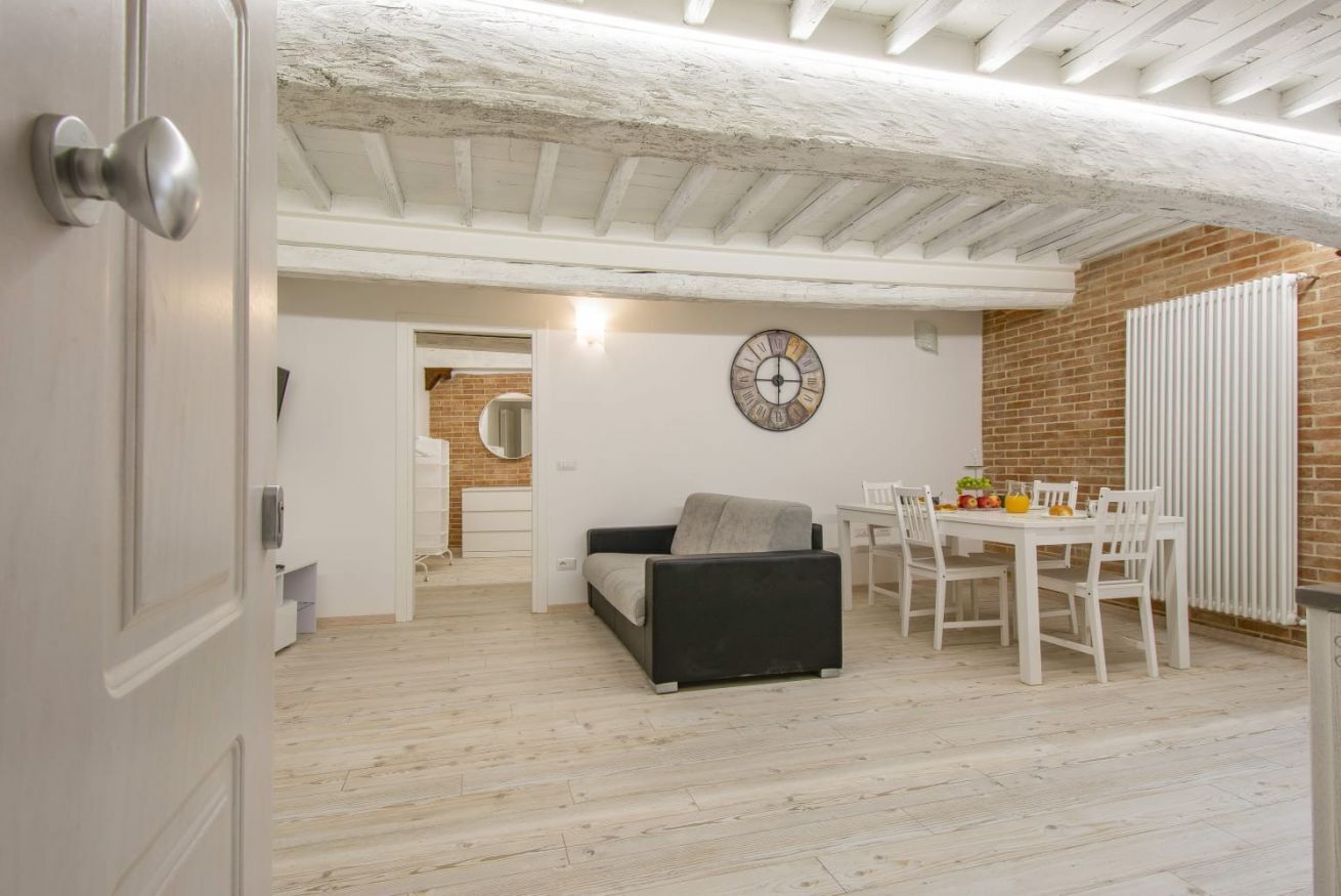 A compact living space with a dining area, a sofa, a clock, and a brick wall.