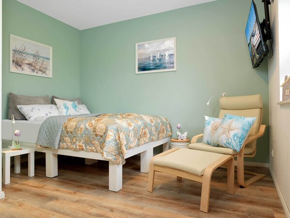 Une chambre à coucher comprenant un lit, une chaise, une table de chevet et deux tableaux accrochés au mur.