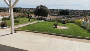 Un espacio al aire libre cubierto con vistas a un jardín ajardinado, muros de piedra y colinas a lo lejos.