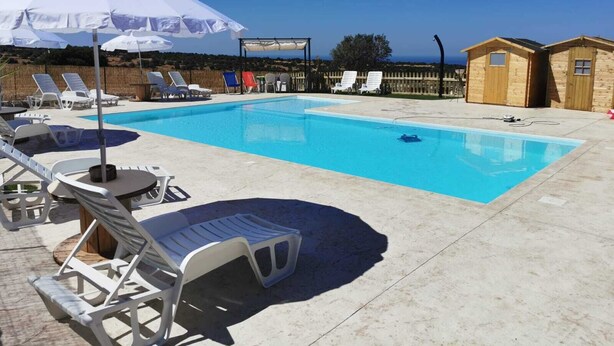 Una piscina con sillones de playa y sombrillas, cabañas de madera y una vista despejada del mar.