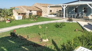 Una casa con jardín, un patio con mobiliario exterior y fachada de piedra.