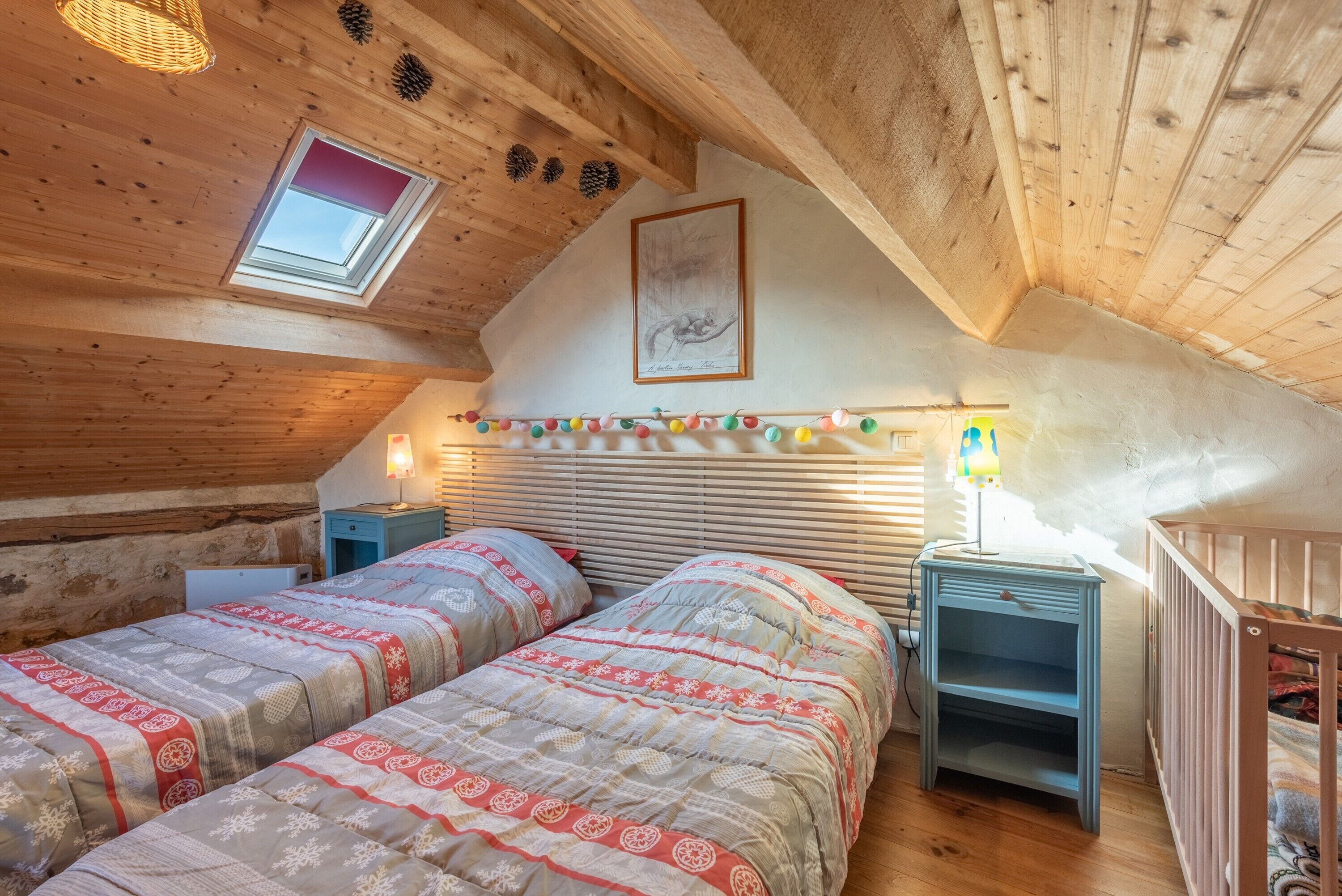 A cozy attic bedroom with two beds, a skylight, a framed picture, and a string of lights.