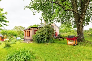 Ein rustikales Holzhaus mit roter Tür, umgeben von üppiger Vegetation und einem großen Baum.