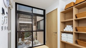 Un bany modern amb una porta de vidre que dona a un jardí, prestatges de fusta amb tovalloles i un paviment de bambú.