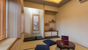 Una habitació japonesa tradicional amb terra de tatami, una taula de tatami, coixins, un petit armari amb un dispositiu vermell i una prestatgeria penjada a la paret.