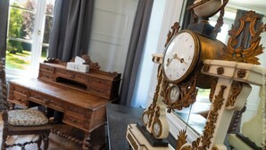 A vintage-style clock with intricate designs and a wooden desk with drawers and a cushioned chair. - Château de Luzières (Conty)
