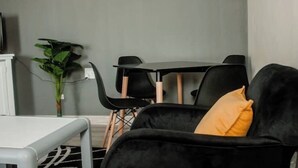 Moderni olohuone, jossa on musta sohva, pieni pöytä ja ruokailutila tuoleineen.
