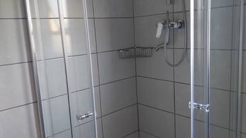 Un petit espace de douche carrelé, doté d’une porte en verre, d’un pommeau de douche à main et d’un robinet fixé au mur.