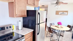 A modern kitchen with wooden cabinets, a stainless steel refrigerator, a built-in oven, and a dining area with a round table and chairs.