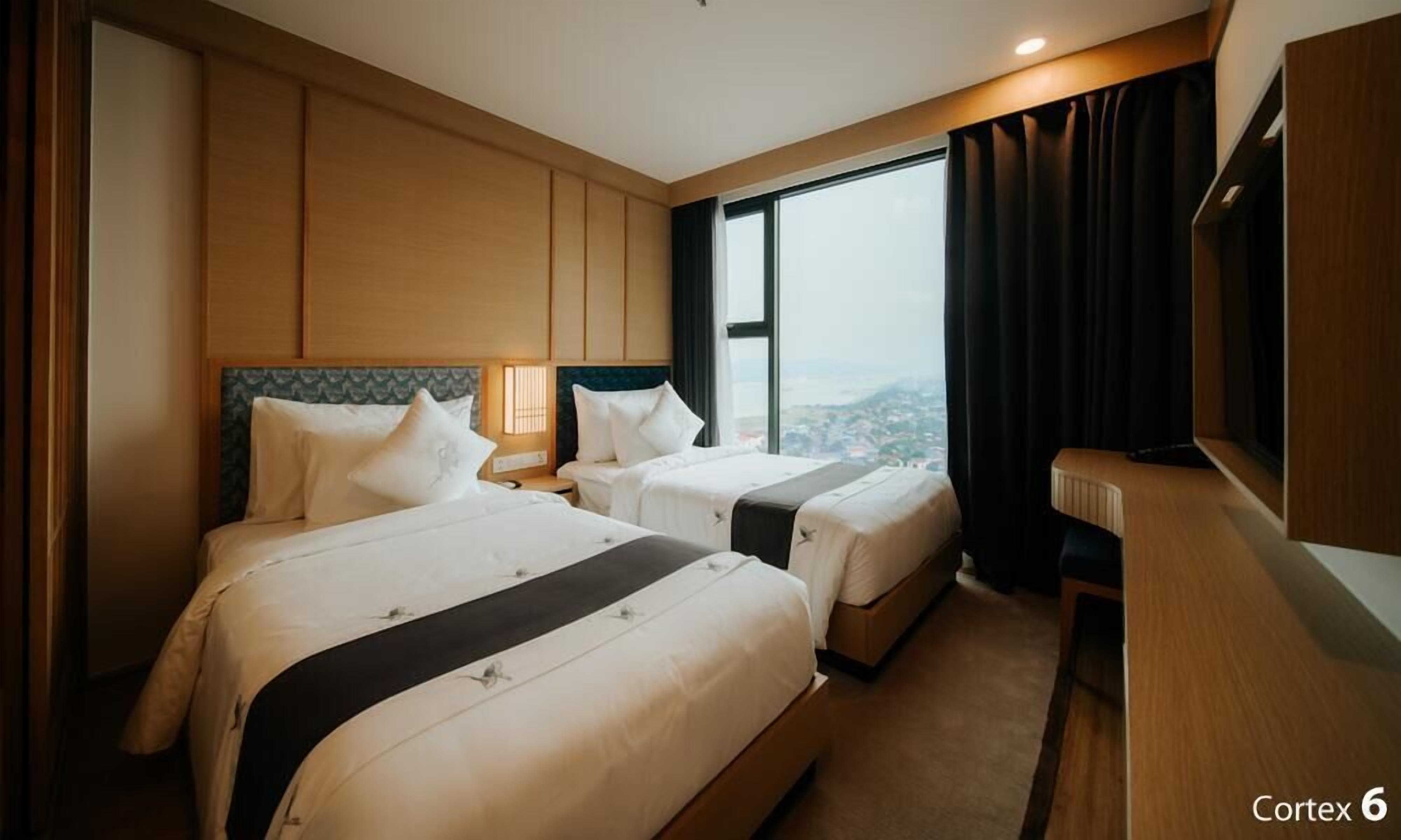 A hotel room with two beds, a large window with a city view, and a television on the right wall.