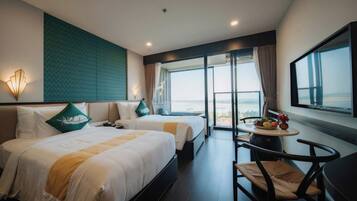 A hotel room with two beds, a dining table with fruit, a chair, and a large window with a view.