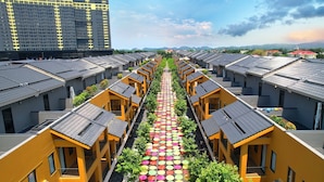 Une rangée de bâtiments jaunes, avec un chemin central bordé de parasols colorés, qui mène à un point de vue lointain sur des montagnes et un grand bâtiment.
