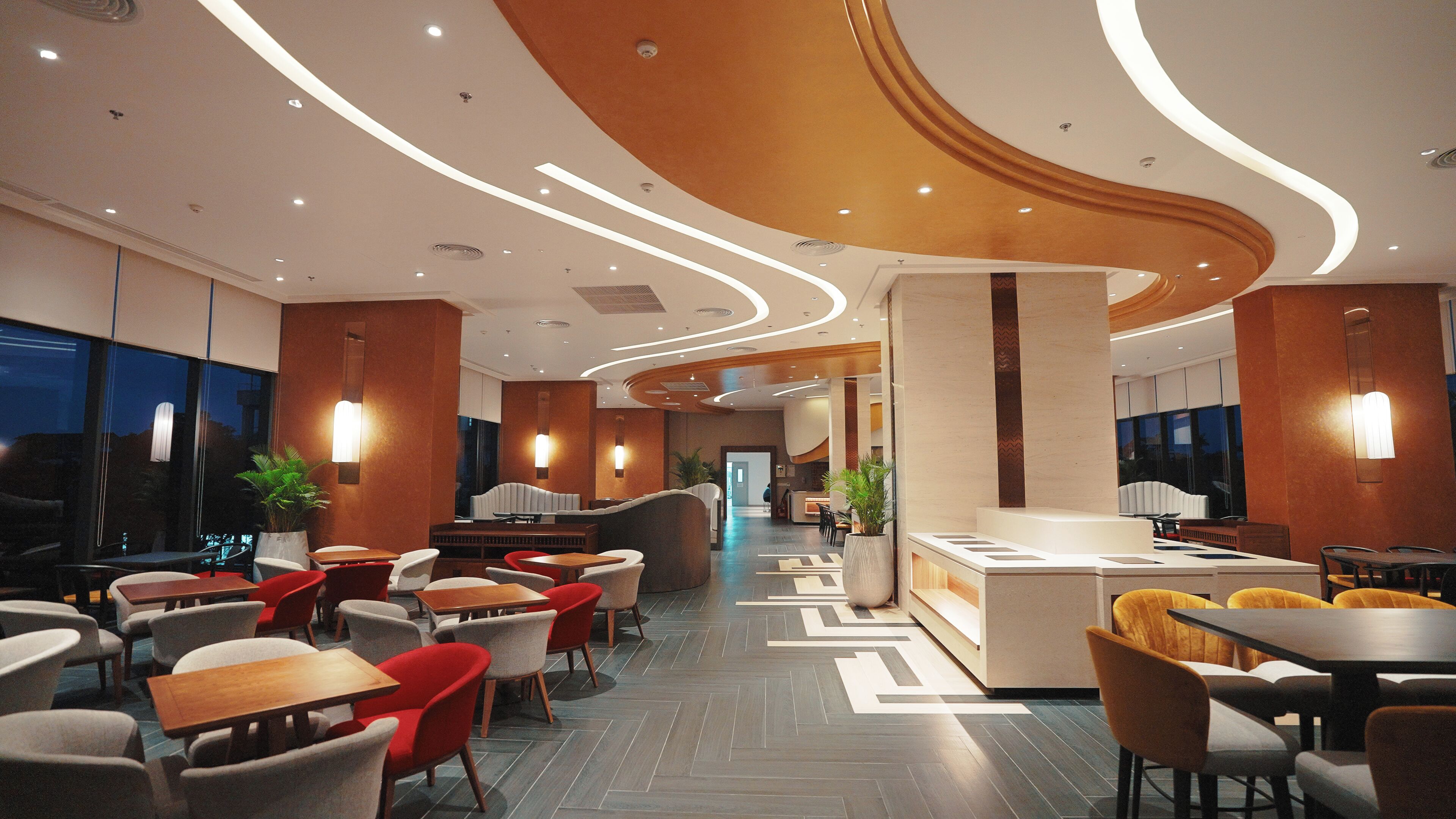 En moderne hotellobby med en central receptionsdisk, flere siddeområder med borde og stole, samt et mønstret gulvdesign.