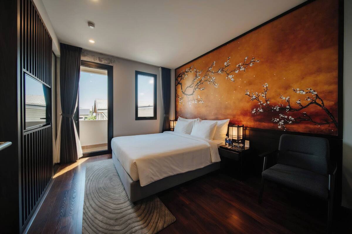 Ein modernes Hotelzimmer mit einem großen Bett, einem Sessel, einem Nachttisch mit Lampe und einem Wandbild.