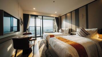 A modern hotel room with two beds, a desk, and a large window offering a city view.