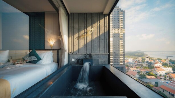 Une chambre d’hôtel moderne dotée d’une grande fenêtre, d’un lit, d’une baignoire avec une cascade décorative et offrant une vue sur la ville.