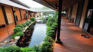 Une allée couverte avec un bassin à carpes koï, un plancher en bois et une vue sur un jardin.