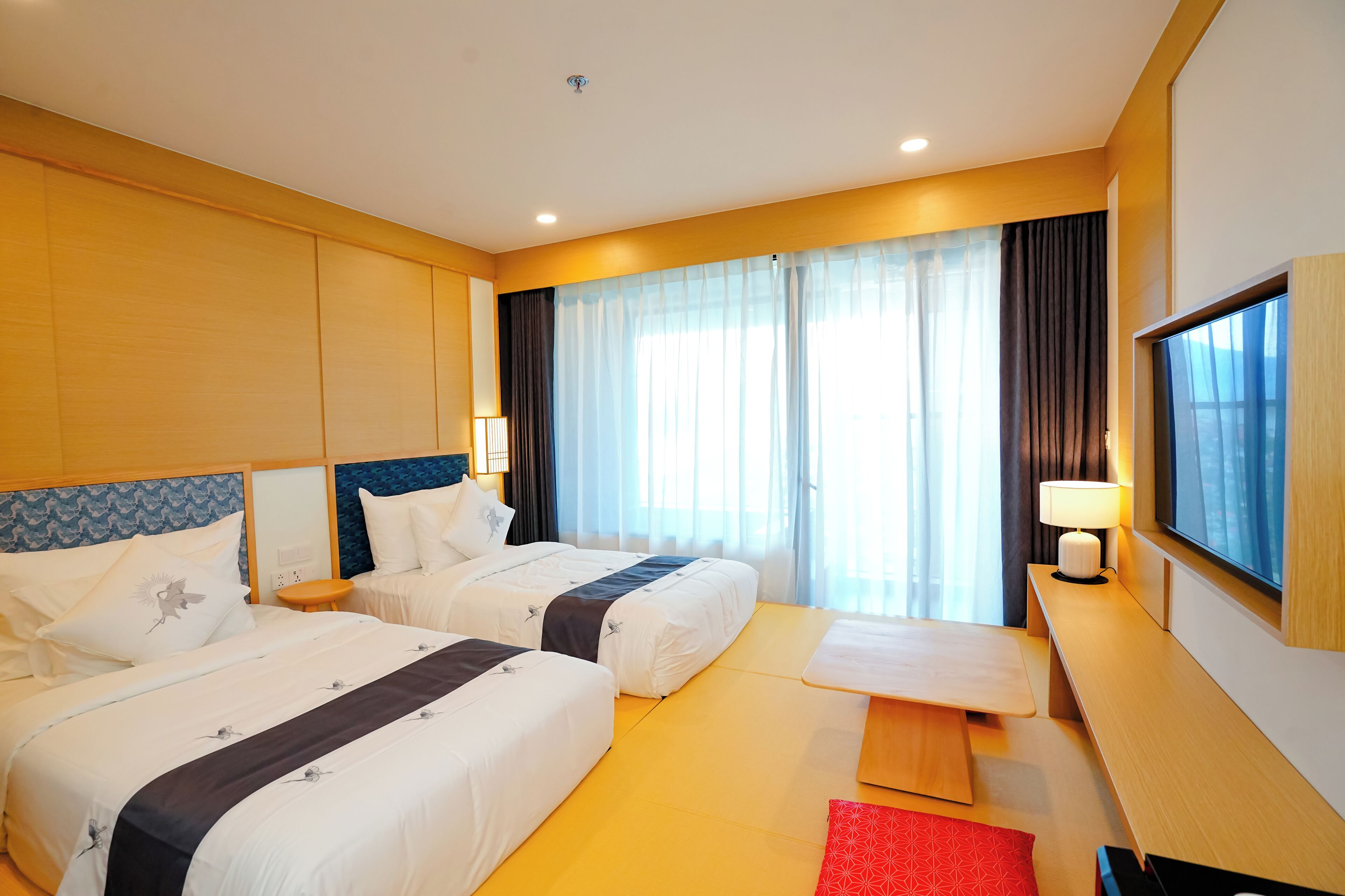 Habitación de hotel con dos camas, televisión, escritorio y ventana con cortinas.