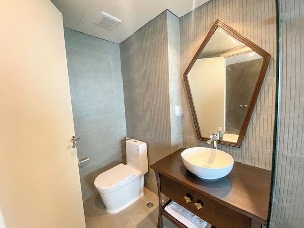 Un baño moderno con un inodoro blanco, un lavamanos con un espejo grande y un perchero para toallas.