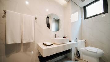 A modern bathroom with a white vanity, a round mirror, a toilet, and a window.