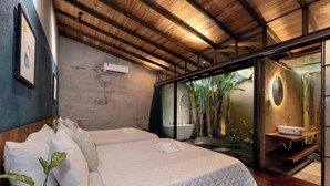 Ein Schlafzimmer mit einem großen Bett, Holzboden und einem Badezimmer mit Waschbecken und Pflanzen.