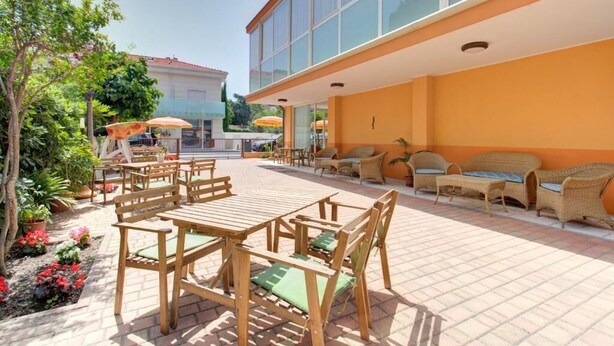 An outdoor patio with wooden tables and chairs, a seating area with wicker furniture, and potted plants.