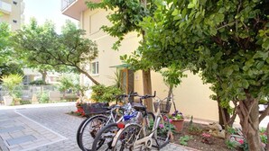 Bicycles parked in a courtyard with a stone pathway, surrounded by potted plants and a tree.