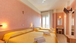A hotel room with three beds, a desk, and a television.