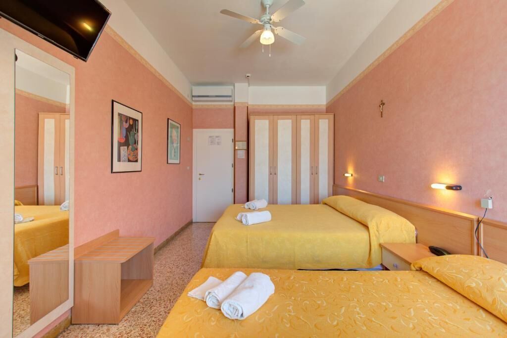 A hotel room with two beds, a ceiling fan, a mirror, and a bedside table.