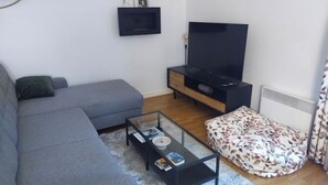 Een moderne woonkamer met een grijze bank, een glazen salontafel, een flatscreen-televisie en een gestreept poef.