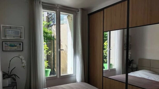 Een slaapkamer met een bed, een schuifdeurkast van hout, een raam met gordijnen en een potplant.