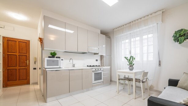 A compact kitchen with white appliances, a dining table with chairs, and a sofa. - "La Casa di Mia" Apartment – Cagliari (Cagliari)