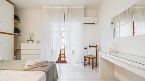 A bedroom with a bed, a chair, a desk, a mirror, and a window with curtains. - "La Casa di Mia" Apartment – Cagliari (Cagliari)