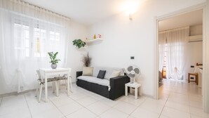 A living room with a sofa, a dining table, a small fan, and a potted plant. - "La Casa di Mia" Apartment – Cagliari (Cagliari)