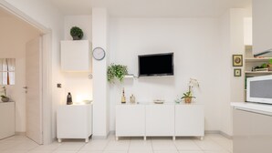 A modern kitchen with white cabinetry, a flat-screen TV mounted above a white console, and a potted plant on the console. - "La Casa di Mia" Apartment – Cagliari (Cagliari)