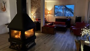 A living room with a wood-burning stove, a sofa, a coffee table, and a TV. - Villa 'Mimosa - Vue Exceptionnelle' with Lake View, Private Terrace and Wi-Fi (Lacanau)