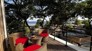 A balcony with wicker furniture and red cushions, overlooking a pool and a view of the sea. - Villa 'Mimosa - Vue Exceptionnelle' with Lake View, Private Terrace and Wi-Fi (Lacanau)