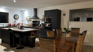A modern kitchen with a central island, black cabinets, and a dining area with wicker chairs. - Villa 'Mimosa - Vue Exceptionnelle' with Lake View, Private Terrace and Wi-Fi (Lacanau)