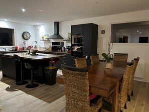 A modern kitchen with a central island, black cabinets, and a dining area with wicker chairs. - Villa 'Mimosa - Vue Exceptionnelle' with Lake View, Private Terrace and Wi-Fi (Lacanau)
