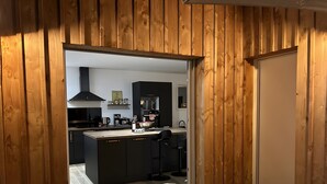 Moderni keittiö, jossa on tummat kaapistot, keskeinen keittiösaareke ja näkymä viereiseen olohuoneeseen.