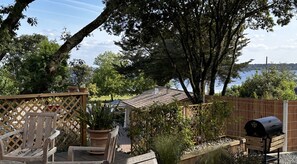 Une terrasse avec une chaise en bois, un barbecue et une vue sur un lac.