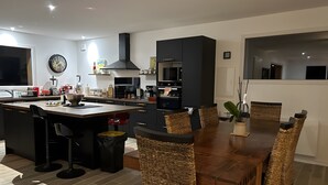 Moderni keittiö, jossa on keskeinen saareke, ruokapöytä ja tuolit.